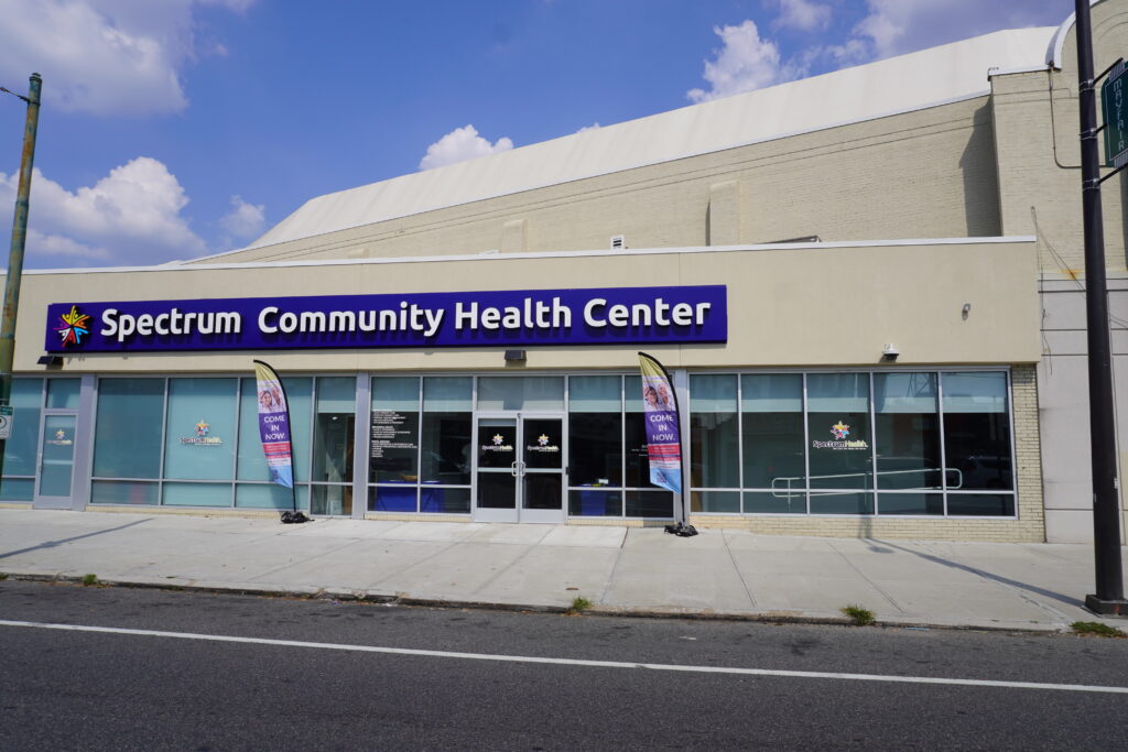 Storefront of a Spectrum Community Health Center with a purple sign above glass doors