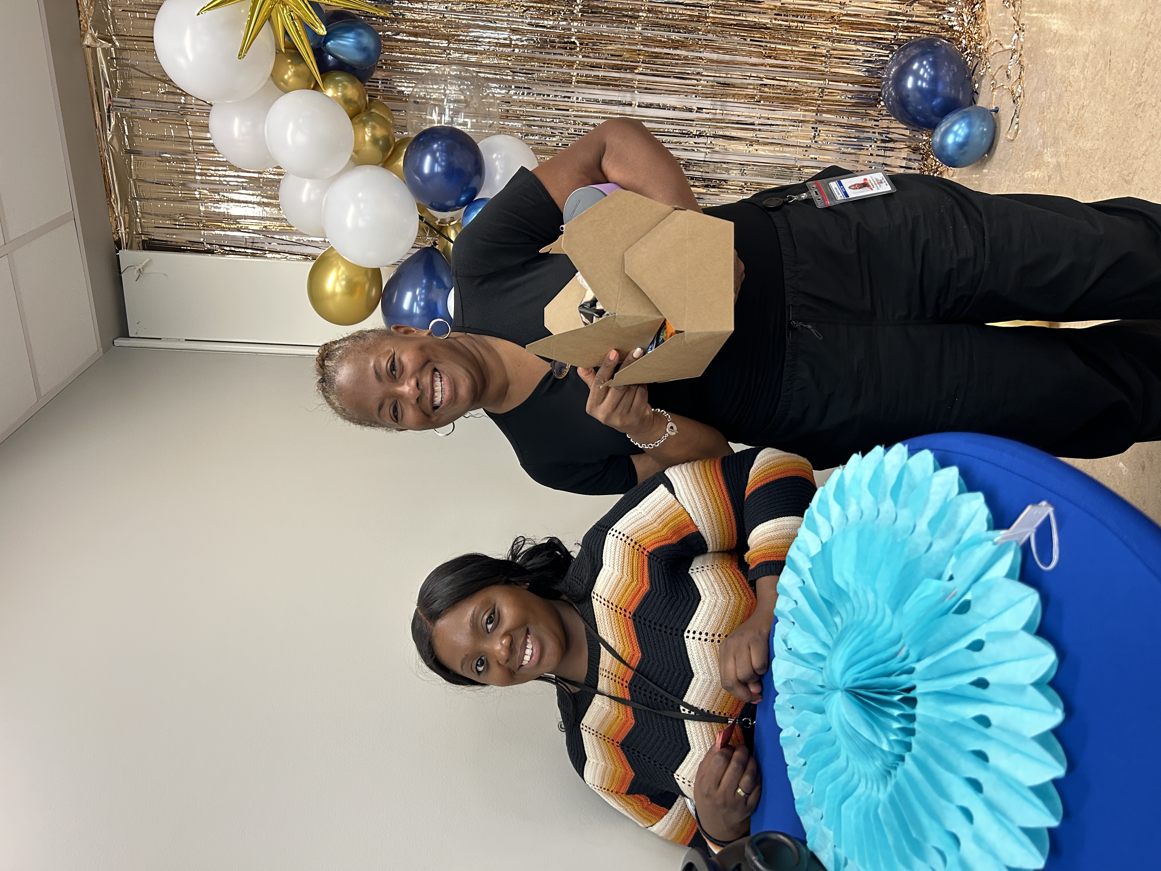 Two staff members smile next to a balloon arch at the barbecue