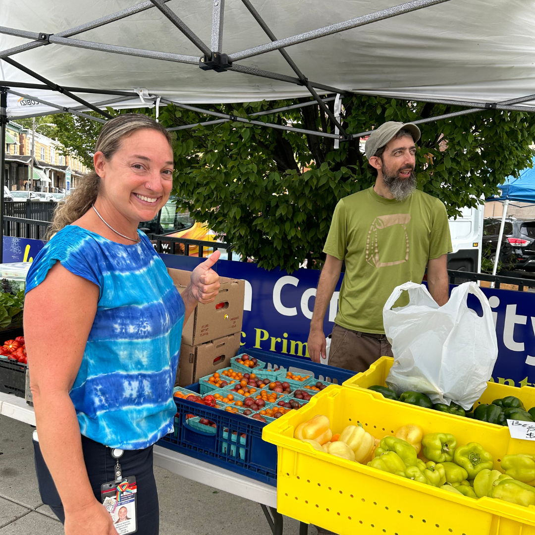 Two people smile next to crates of produce