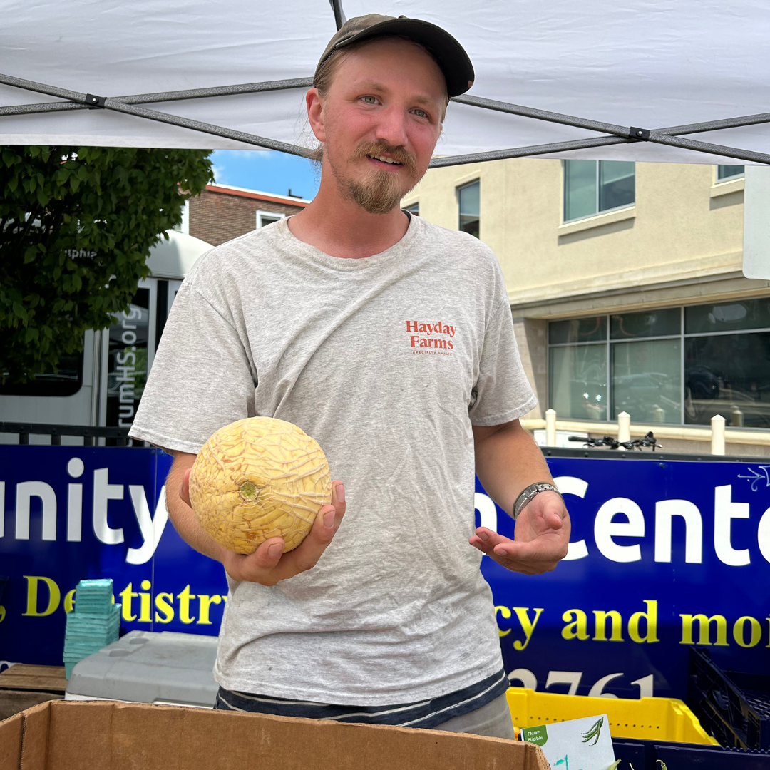 A man holds up a melon at the produce stand
