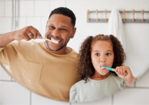 father and young daughter brushing their teeth in the bathroom mirror