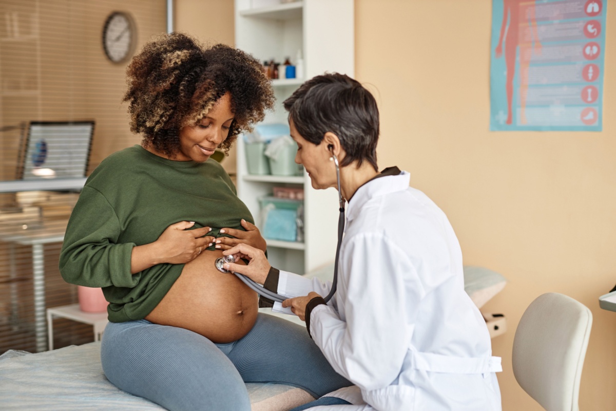 pregnant woman sitting on the exam table with her shirt lifted as the doctor listens to her baby's heartbeat