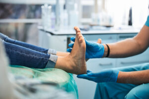close up view of a doctor wearing blue gloves and examining the bare foot of a woman whose pant legs are rolled up