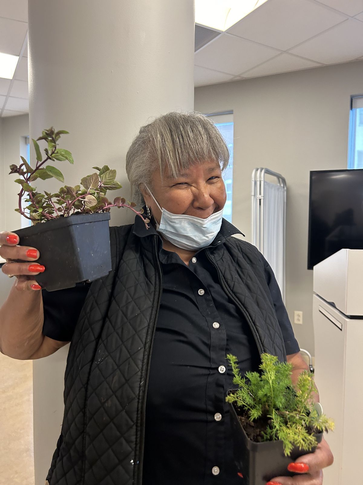 A woman in a face mask holds two small potted plants