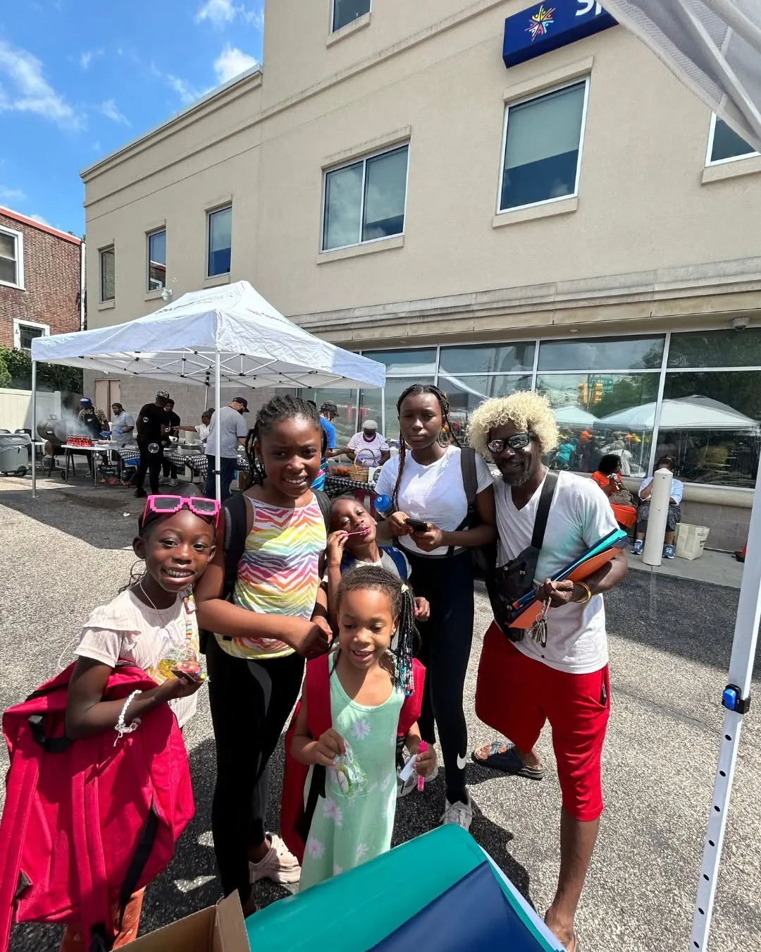 A group of kids smile with new backpacks outside the health center.
