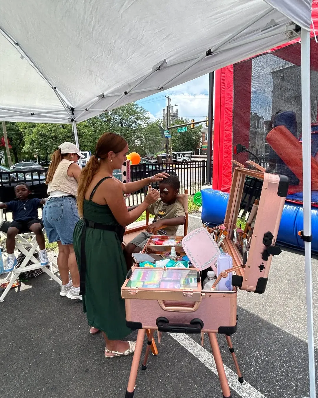 A face painter decorates a child’s face under a tent.