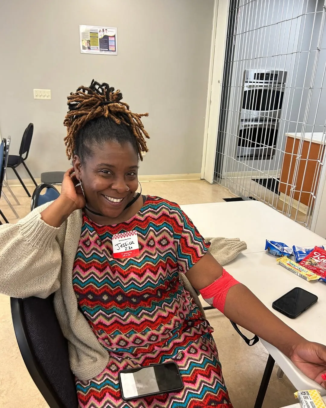 A smiling donor relaxes with a red wrap on her arm after giving blood.
