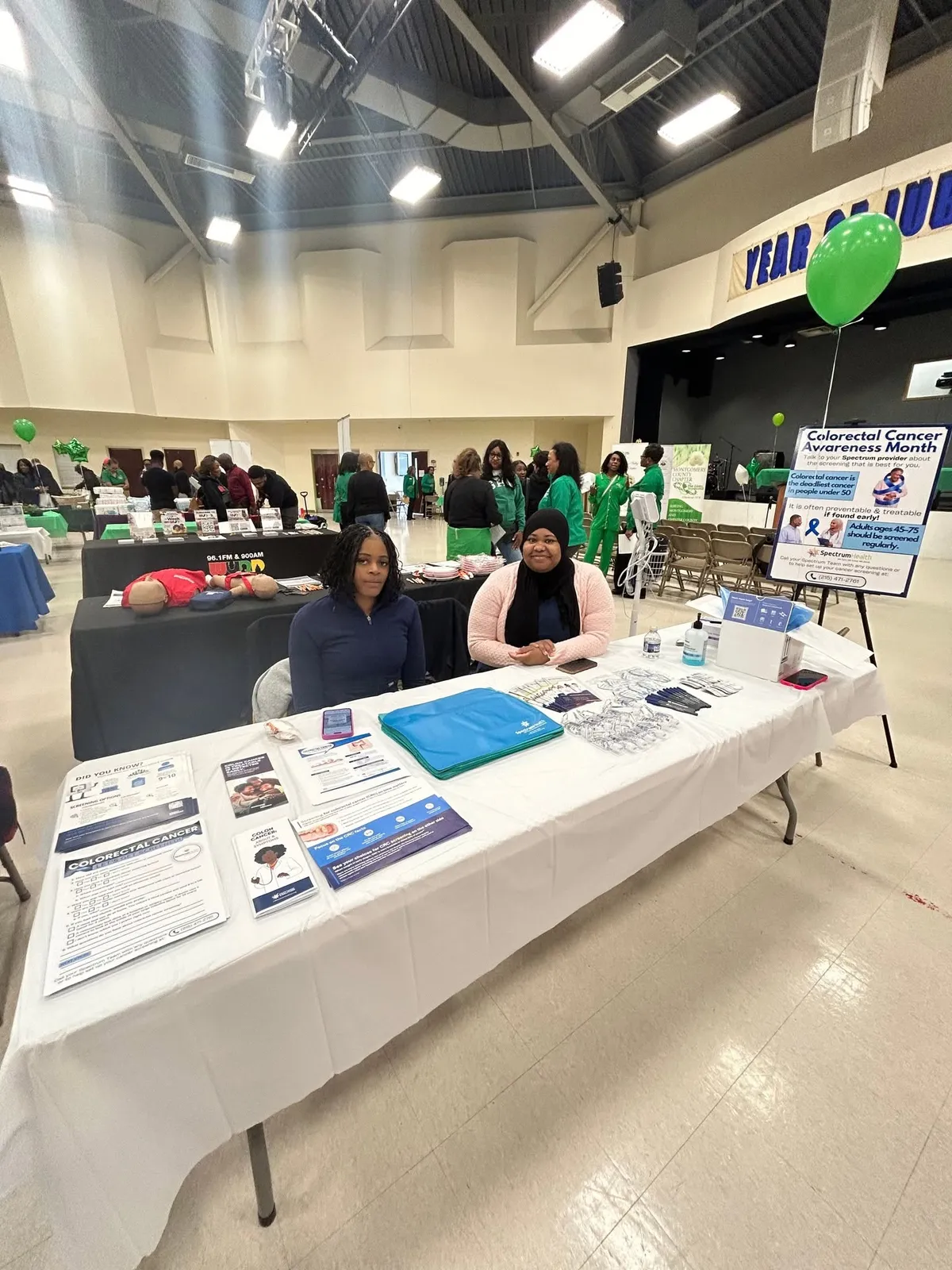 The Spectrum booth with flyers and a sign about colon cancer screening in a big event hall.