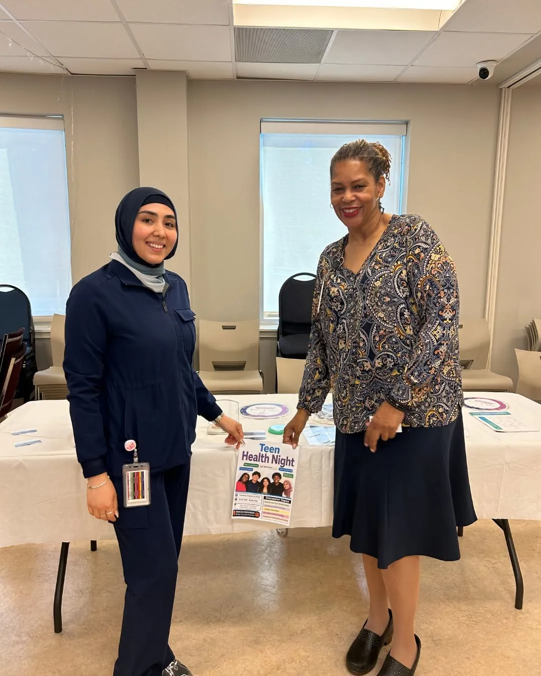 Two staff members smile and hold a Teen Health Night flyer.