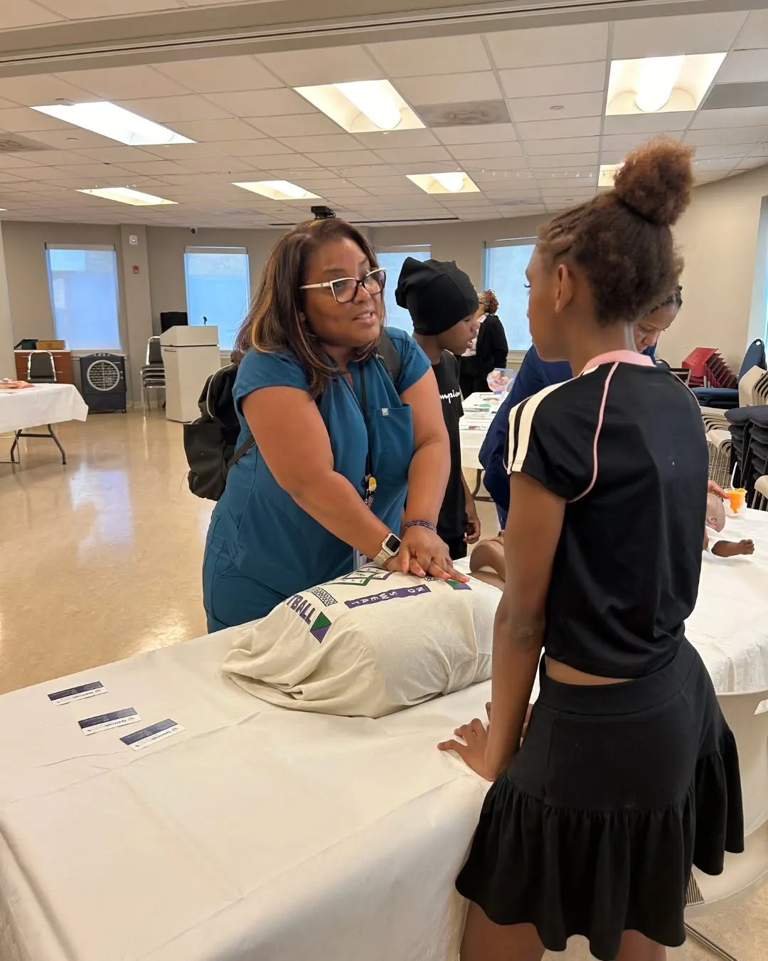A staff member helps a teen practice CPR on a training dummy.